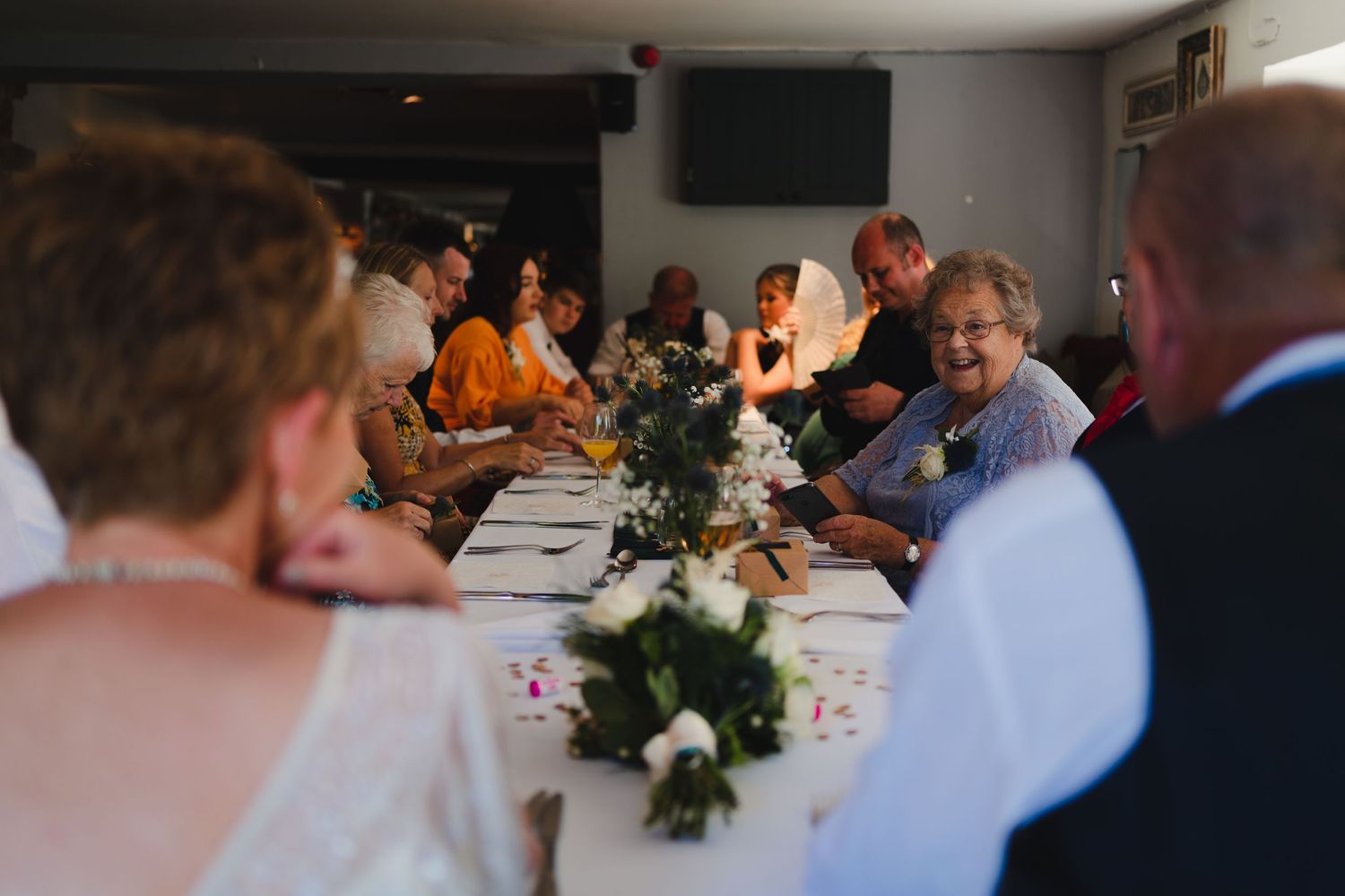 Wedding reception dinner table with floral centerpieces and guests.