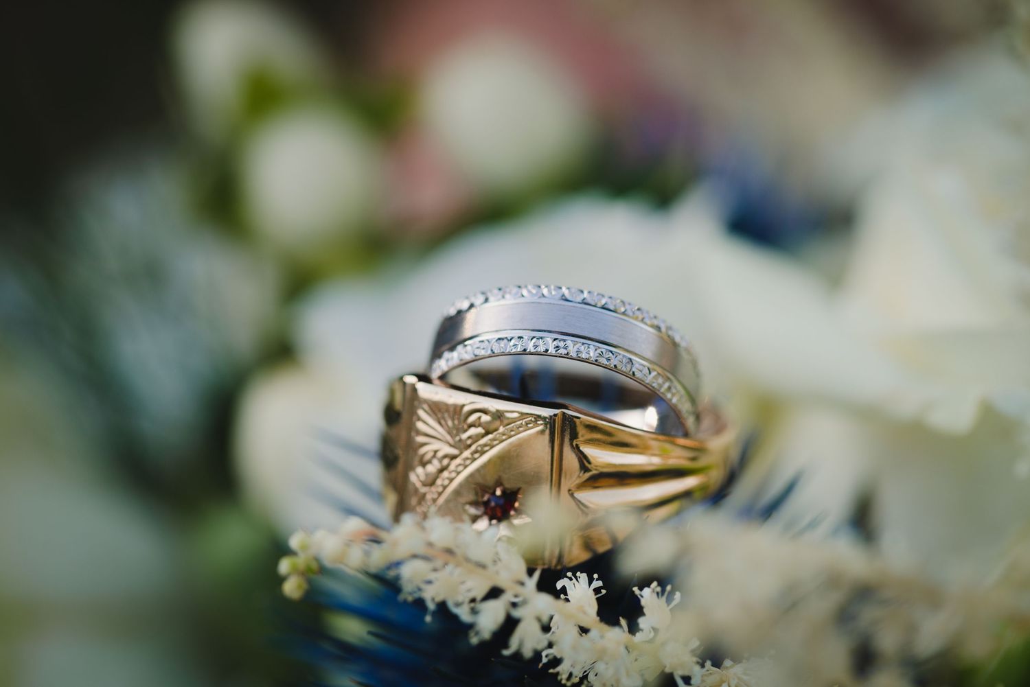 Gold and silver wedding ring with intricate details photographed among white flowers.