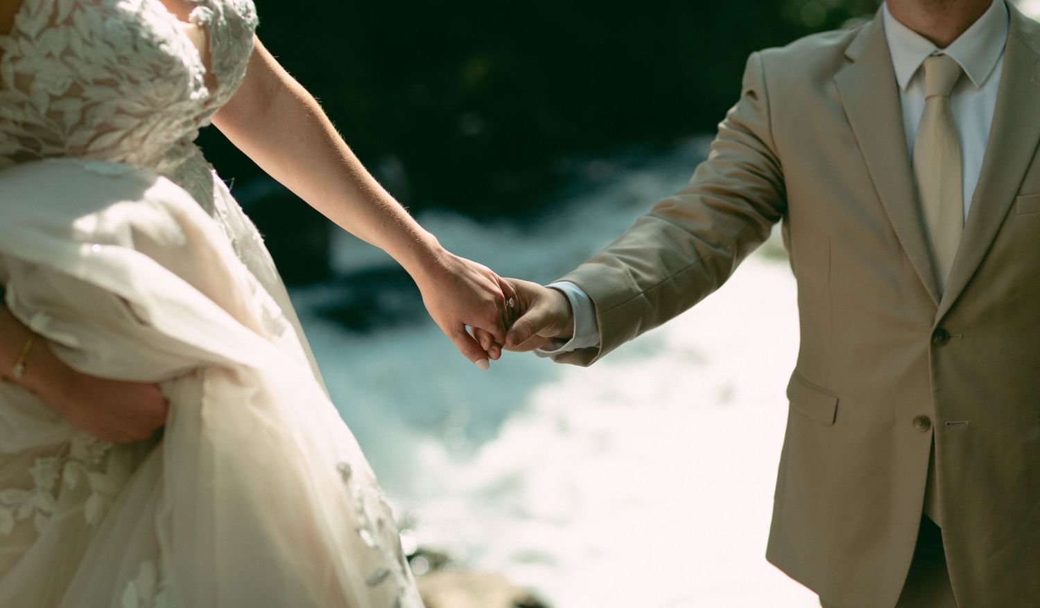 Two hands clasped together against a dreamy background during a wedding ceremony.