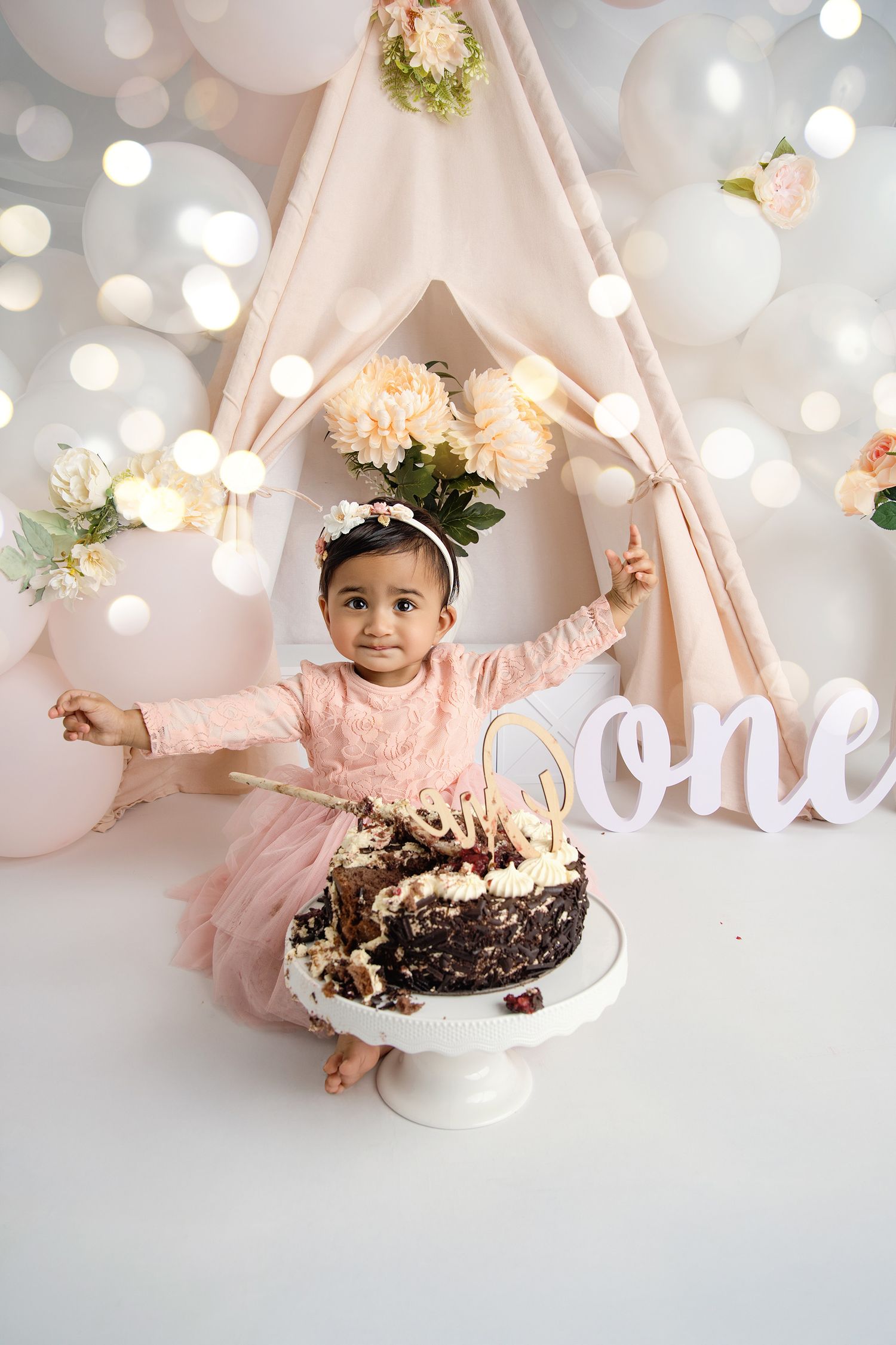 First birthday celebration with cake and pink teepee tent decorated with flowers.