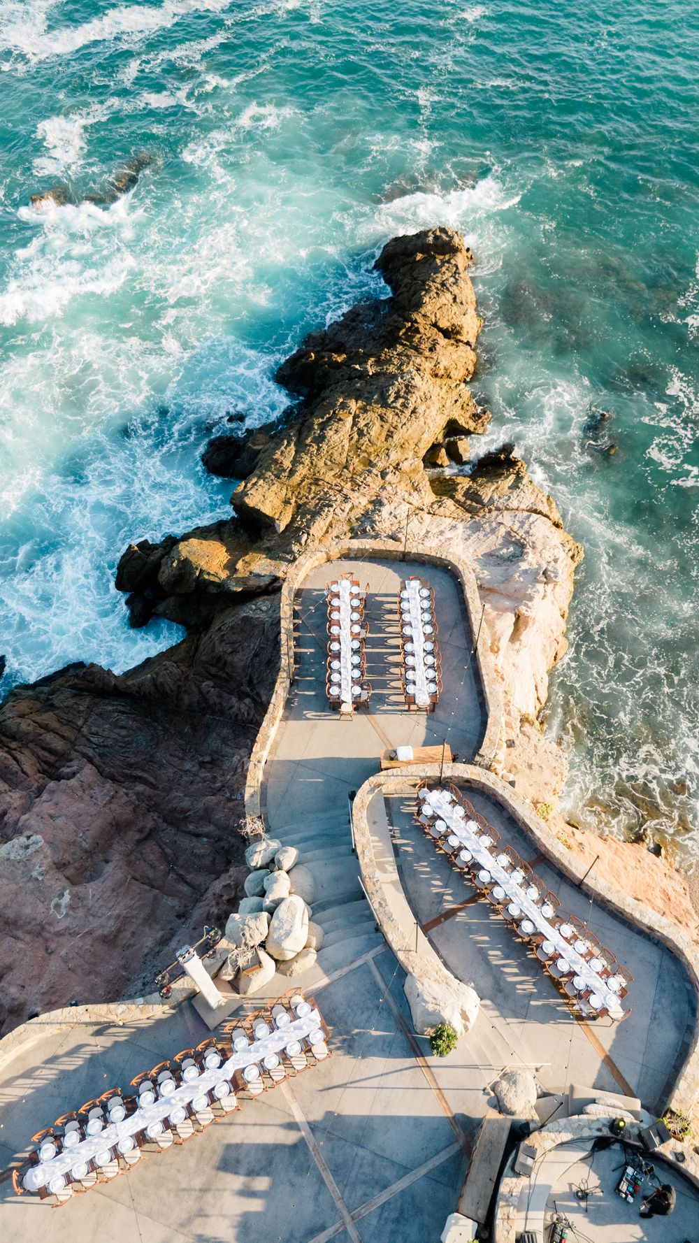 Aerial view of an oceanside wedding reception venue with white tables set along rocky cliffs.