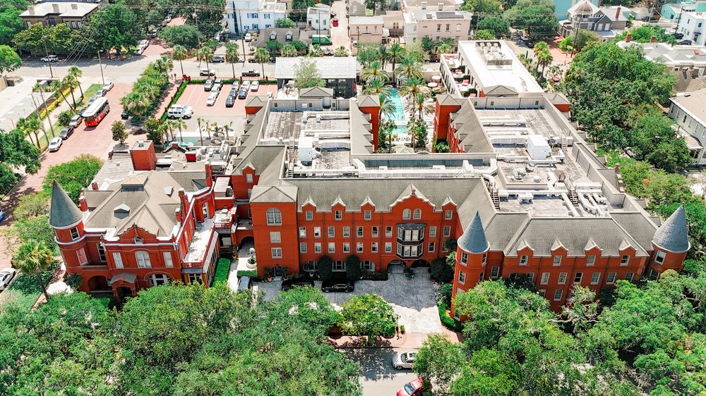 Aerial view of a large red brick colonial-style building complex surrounded by lush green trees in an urban setting.