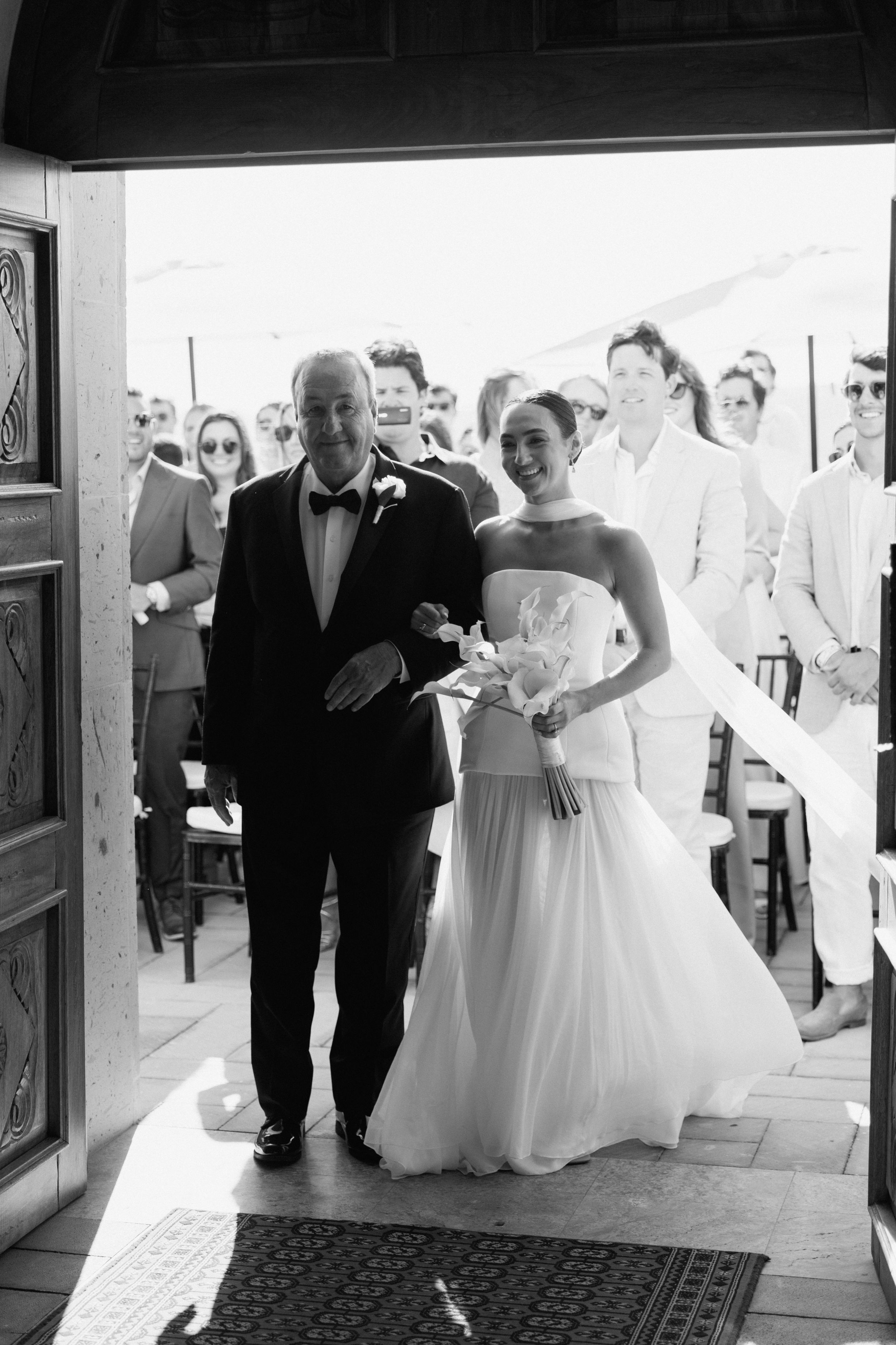 Bride walks down the aisle with her father in a stunning strapless wedding gown in black and white.