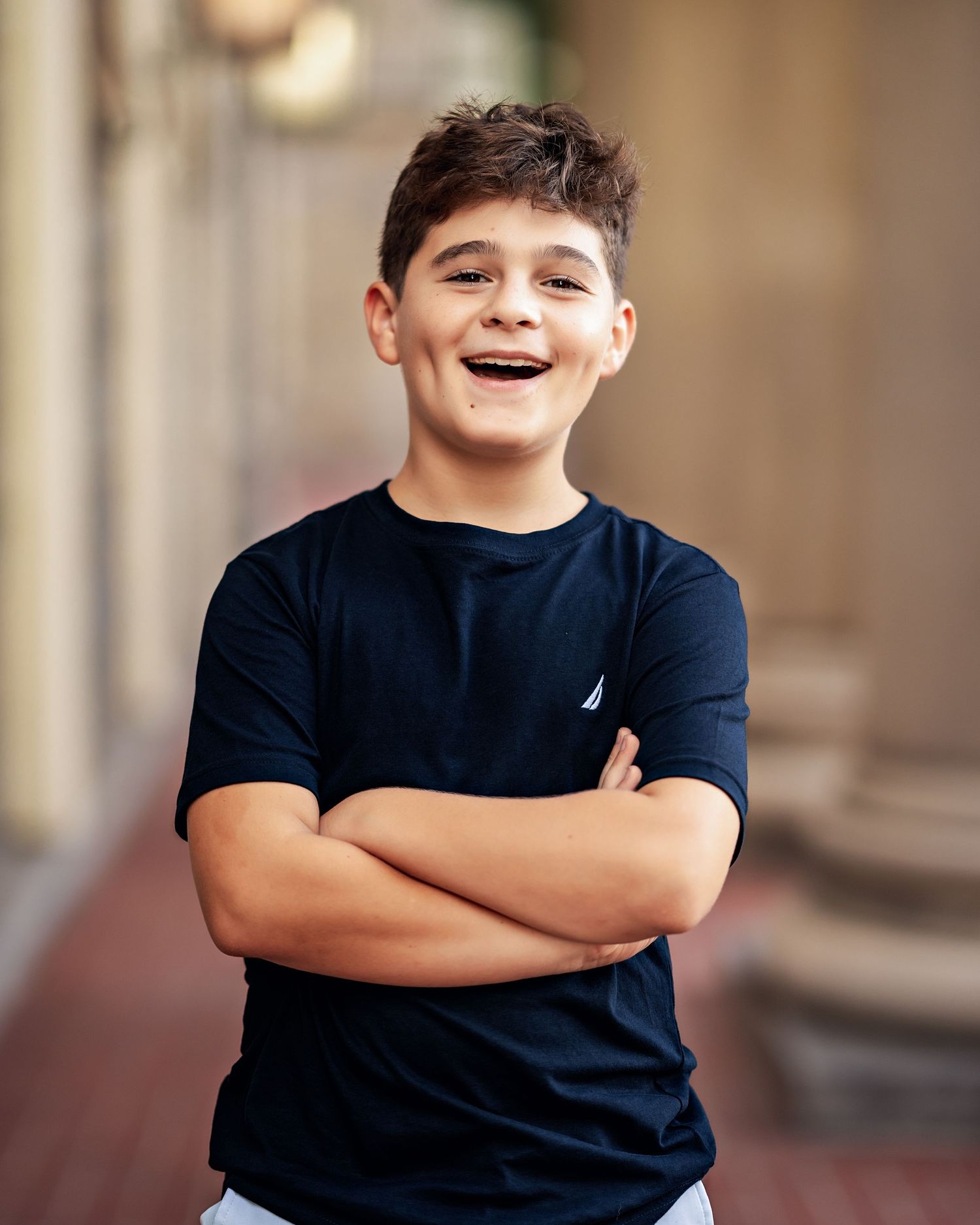 A joyful person in a navy blue t-shirt with a small logo stands with crossed arms while smiling warmly.