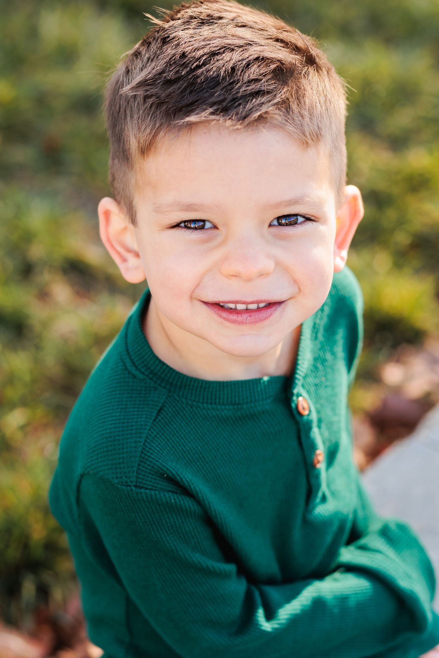 A young child wearing an emerald green sweater smiles warmly at the camera.