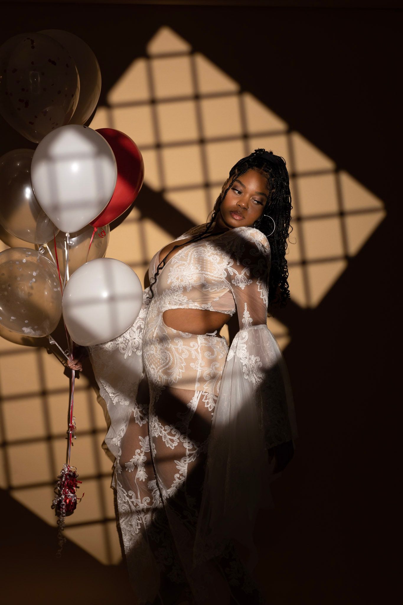 Moody portrait in warm lighting with white and red balloons casting geometric window shadows on the wall.