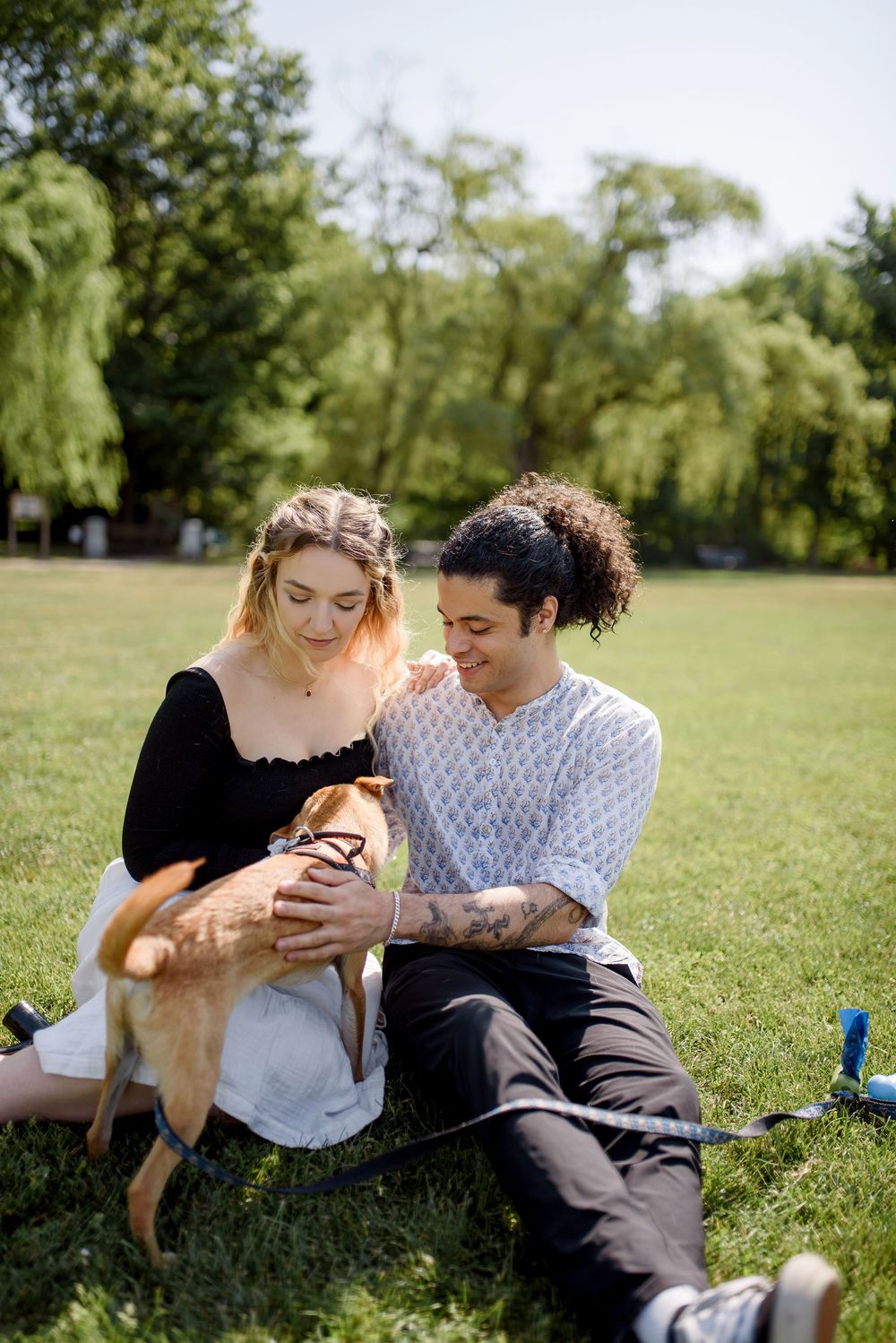 Two people relax together on grass while enjoying a sunny afternoon in a park.