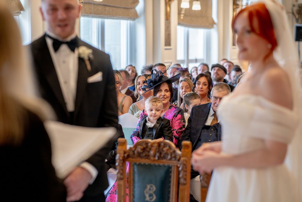 Wedding guests smile joyfully as they watch a ceremony taking place in an elegant indoor venue.