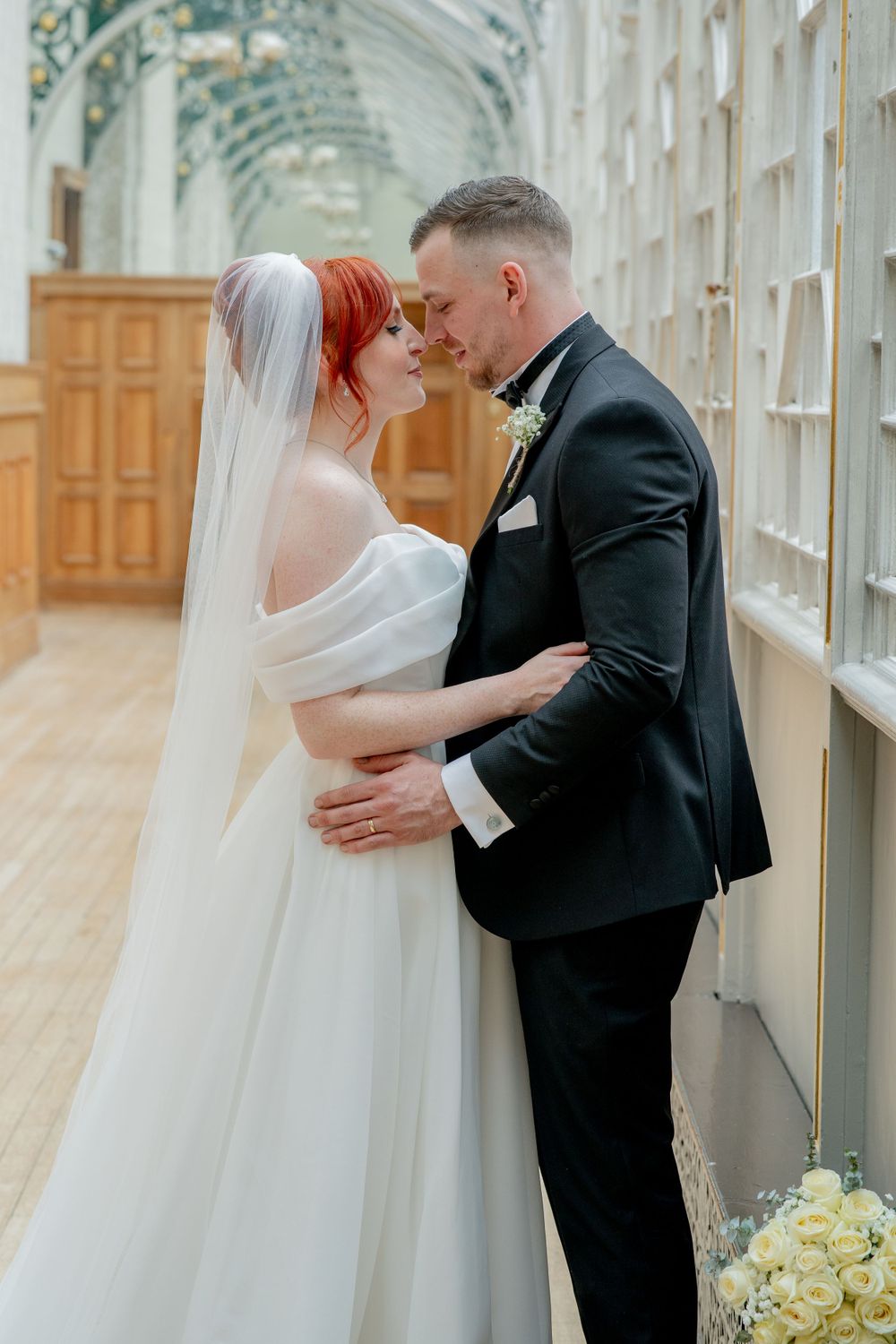 Intimate wedding moment captured in an elegant corridor with arched windows and natural light.