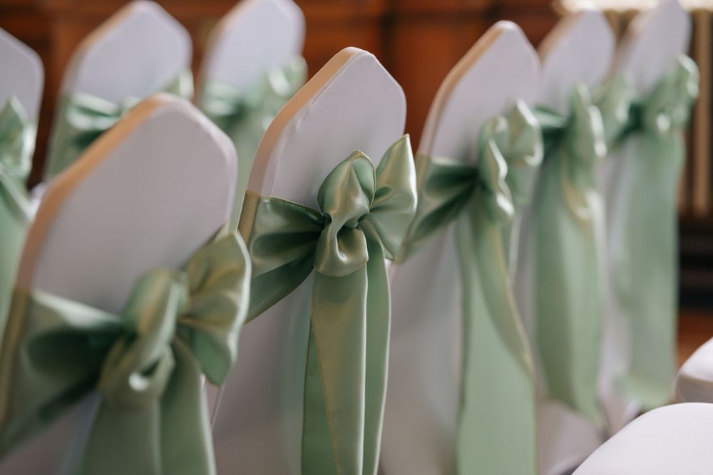 White chair covers decorated with elegant mint green satin bows lined up for a formal event.