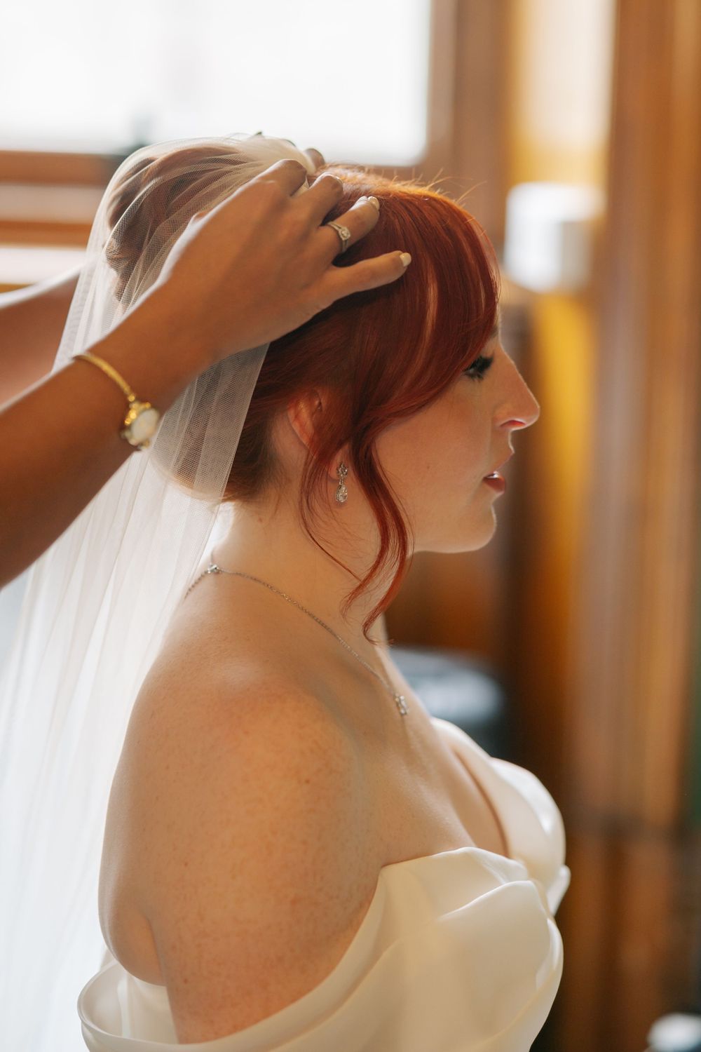 A bride in a white wedding dress has her veil adjusted while getting ready for her ceremony.