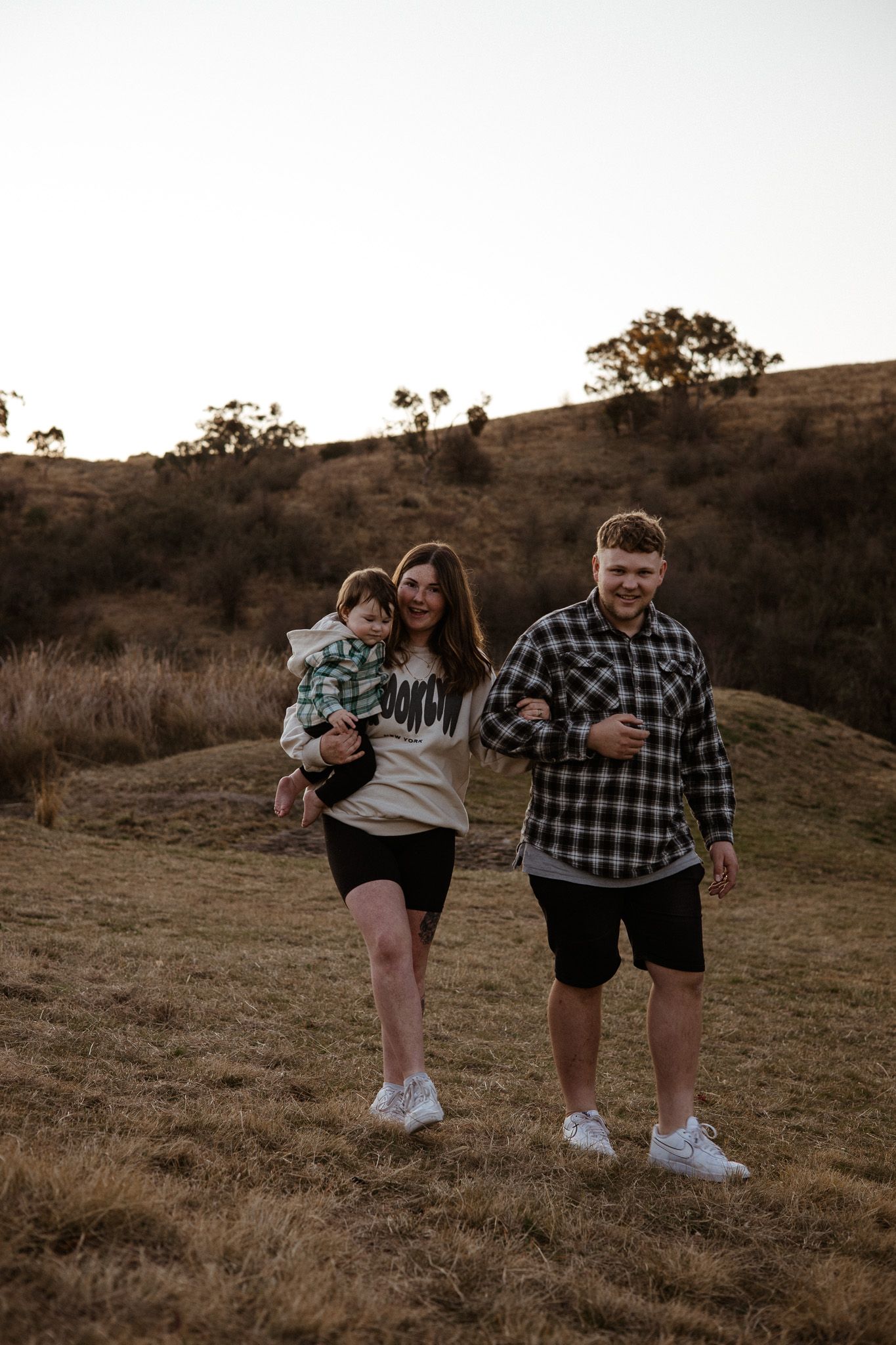 Family walking together at sunset on a grassy hillside with trees in background.