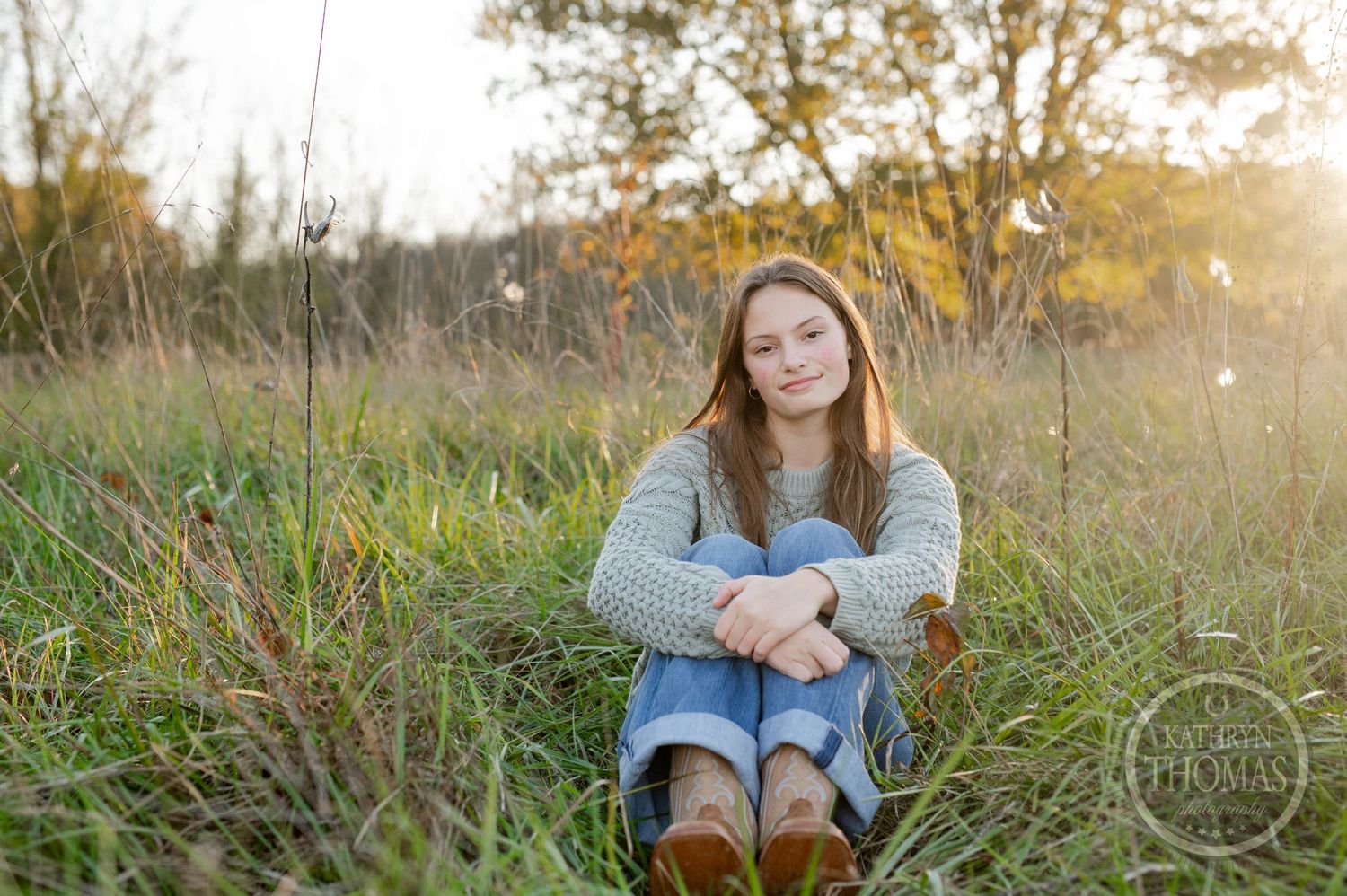 Peaceful autumn portrait of someone sitting in tall grass at sunset wearing a gray sweater.