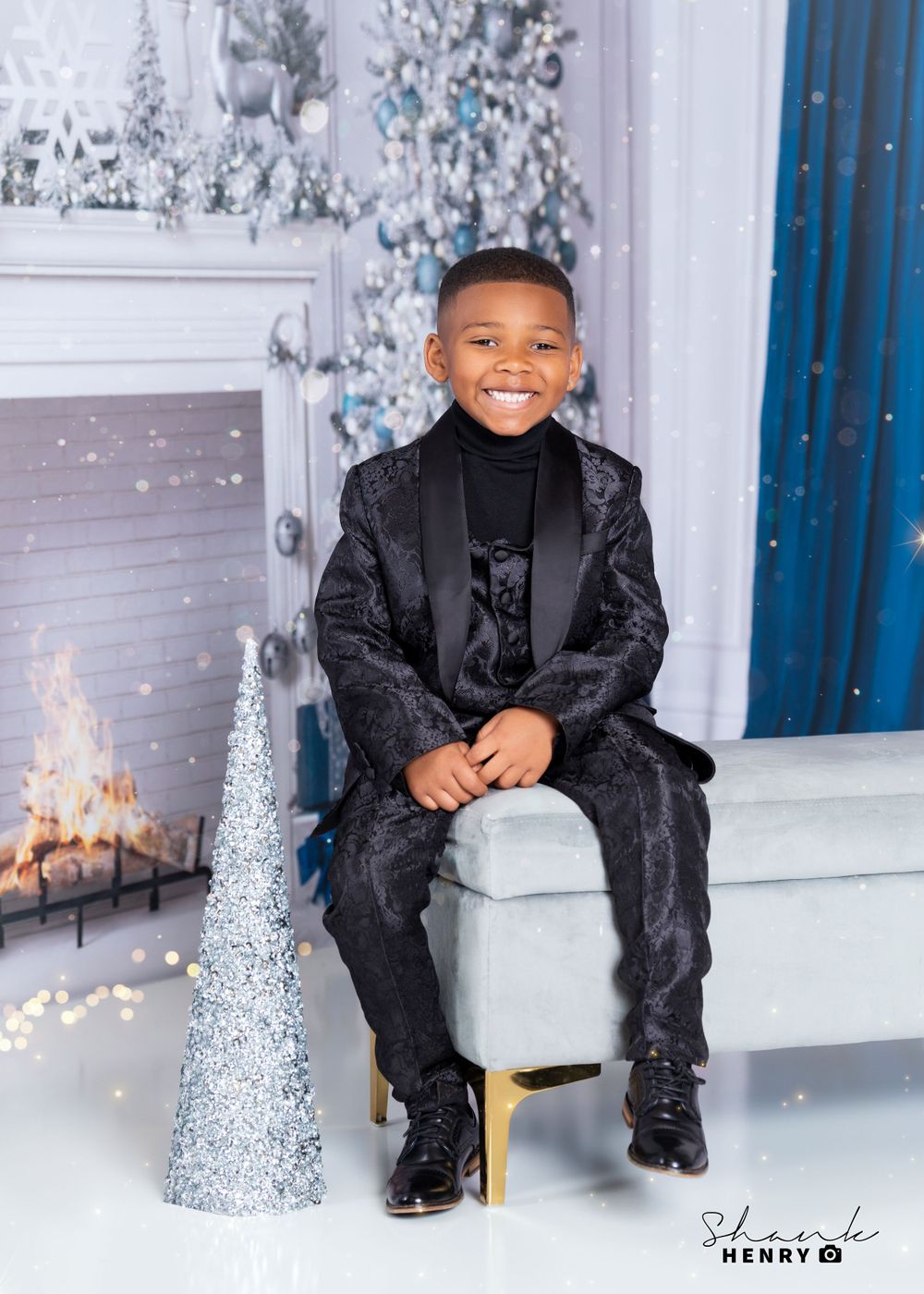 Elegant holiday portrait in black velvet suit against winter wonderland backdrop with silver decorations.
