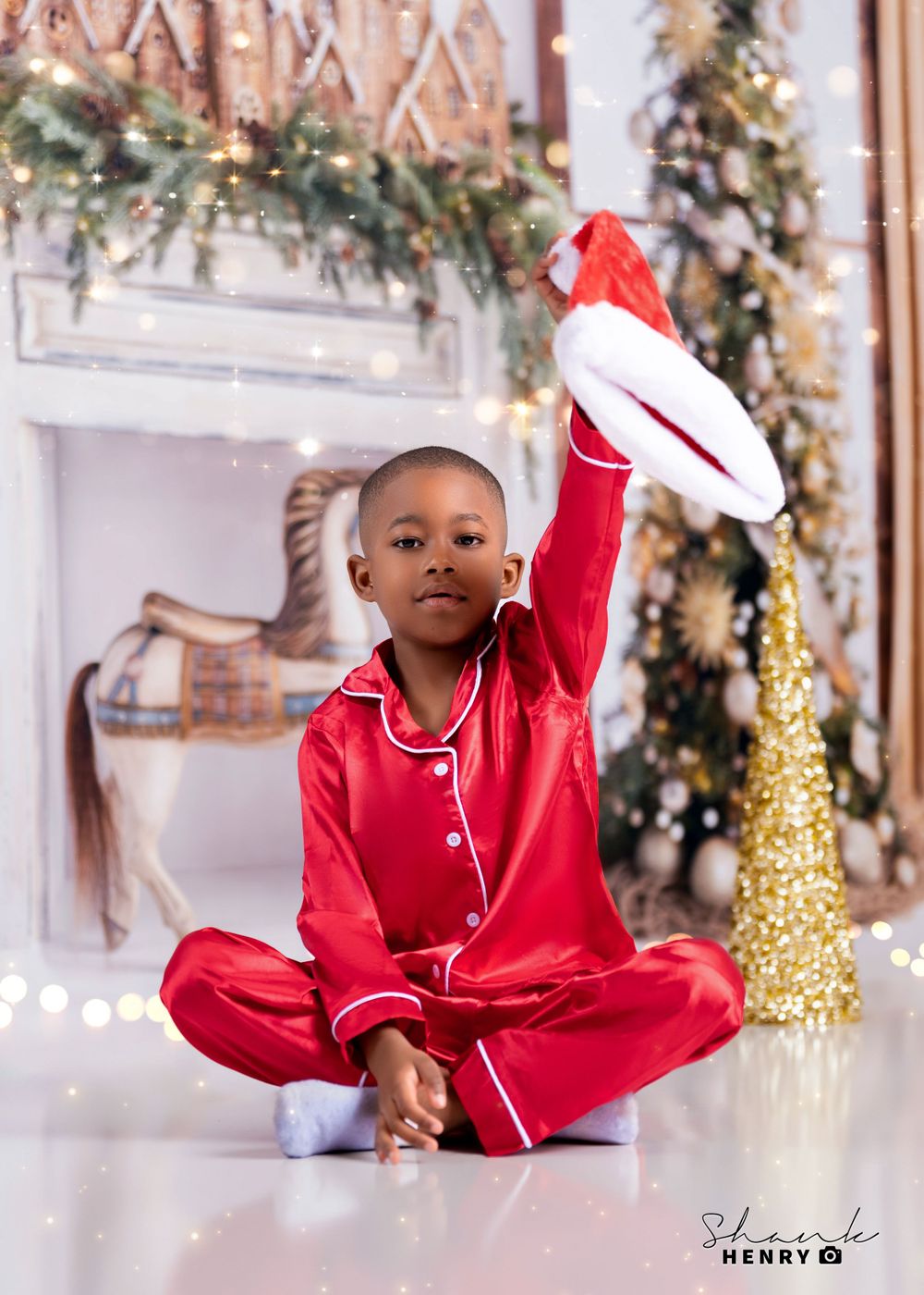 Child in red silk pajamas poses playfully in front of Christmas decorations.