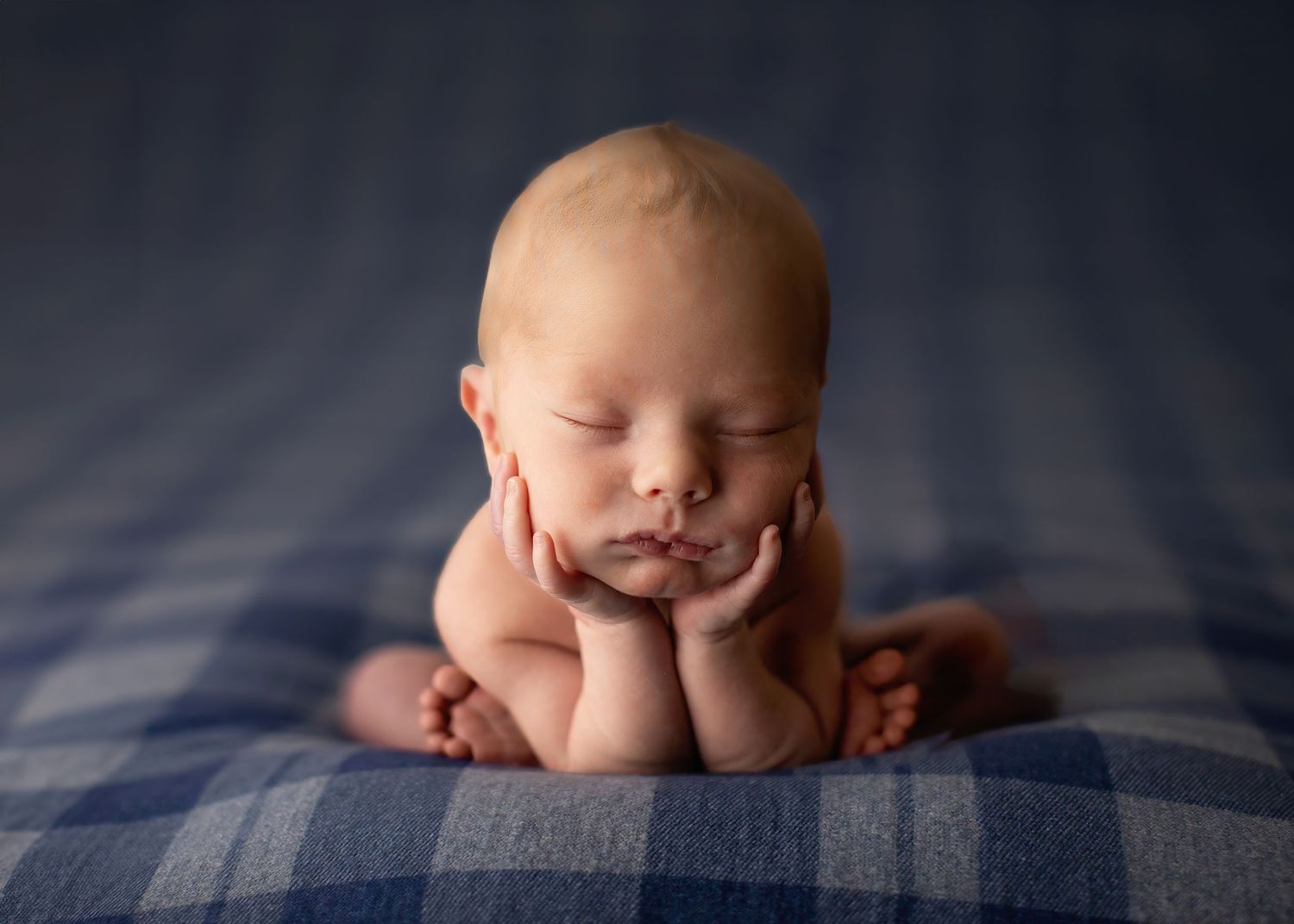 Peaceful sleeping newborn posed in a froggy position on blue striped blanket during studio photoshoot.