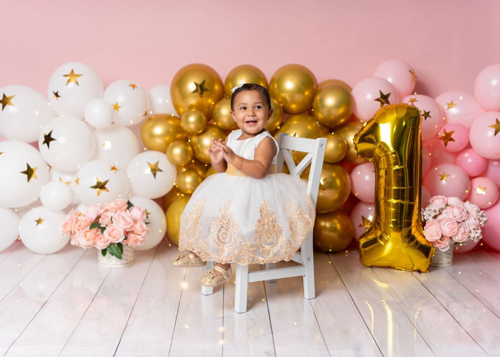 First birthday celebration setup with pink and gold balloon arch and decorations.