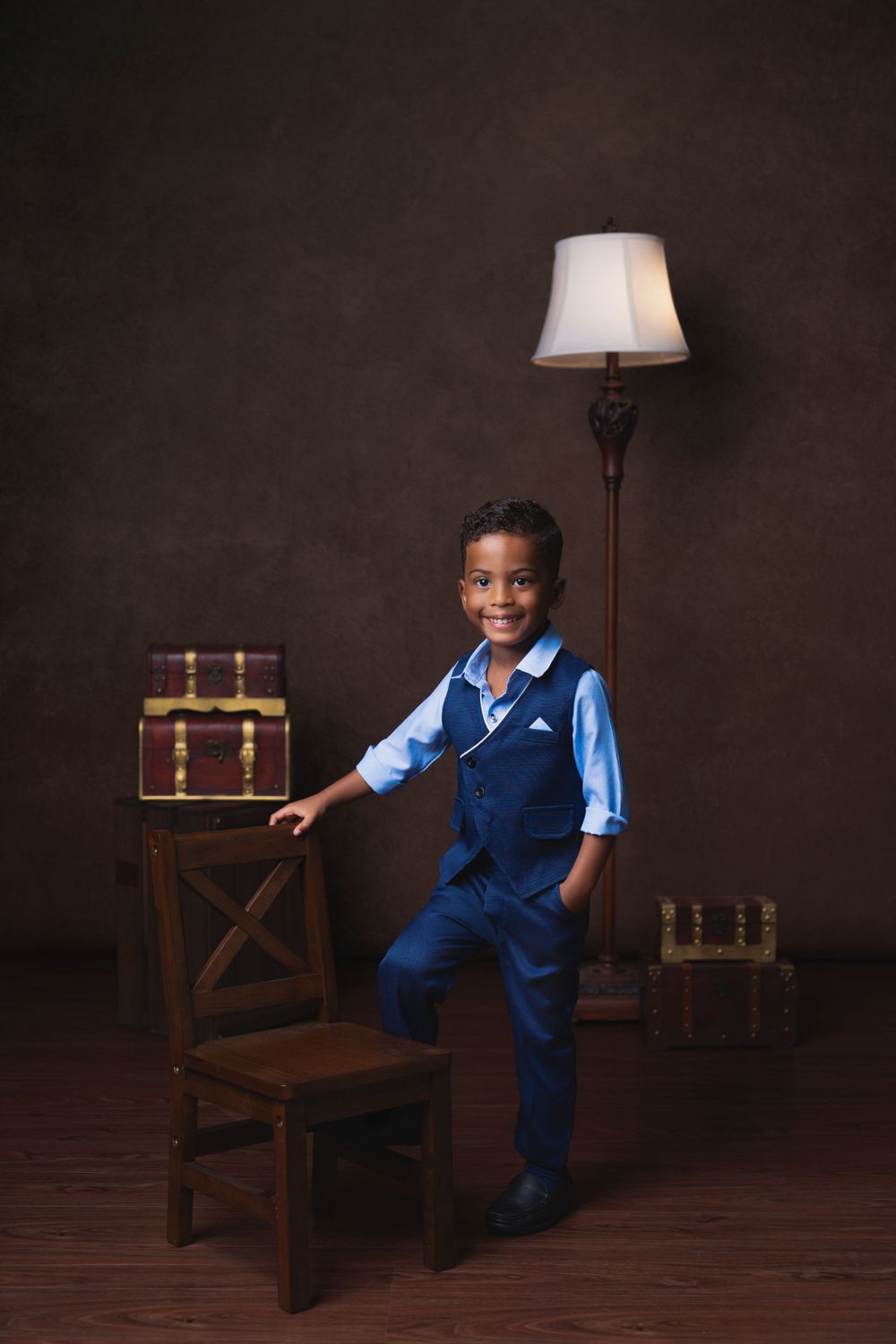 Classic portrait style photo with wooden furniture and lamp against moody brown backdrop.
