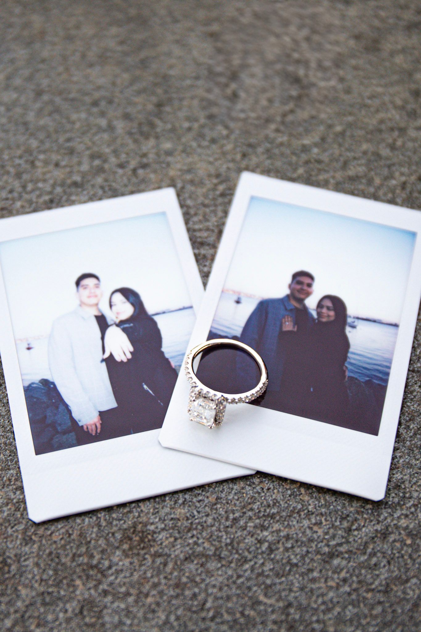 Two polaroid photos and an engagement ring arranged on a grey carpet.