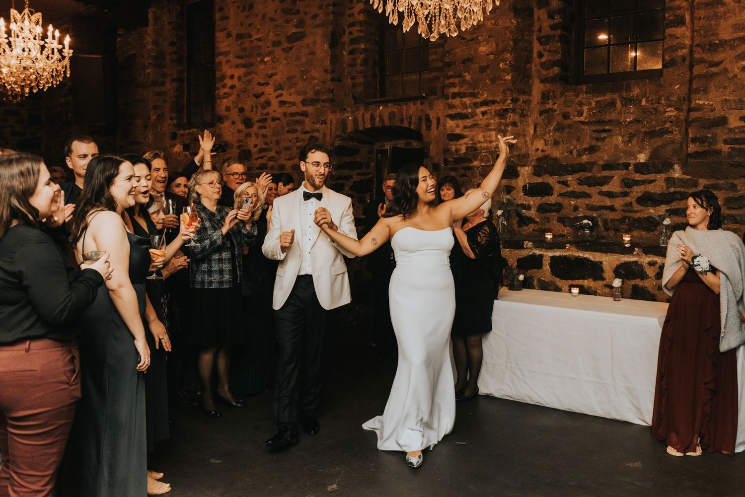 A couple dances together during their wedding reception in a rustic brick venue with elegant crystal chandeliers.