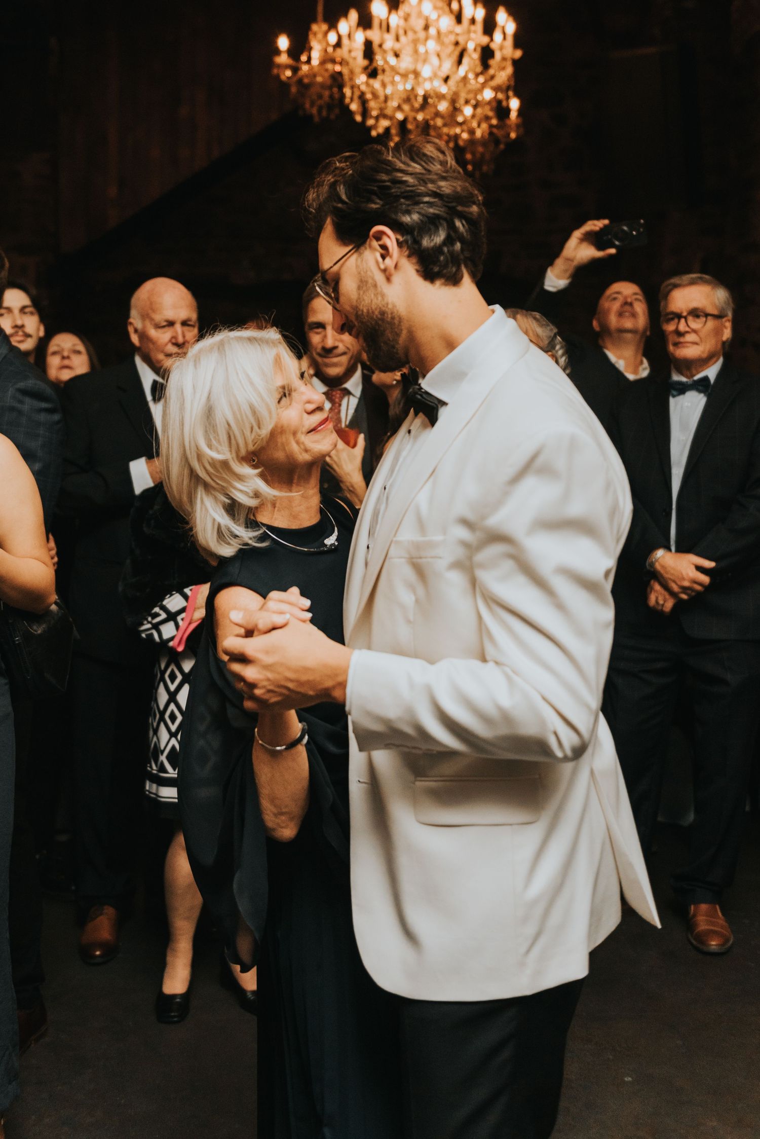 A couple shares a tender moment dancing together at an elegant wedding reception under a crystal chandelier.