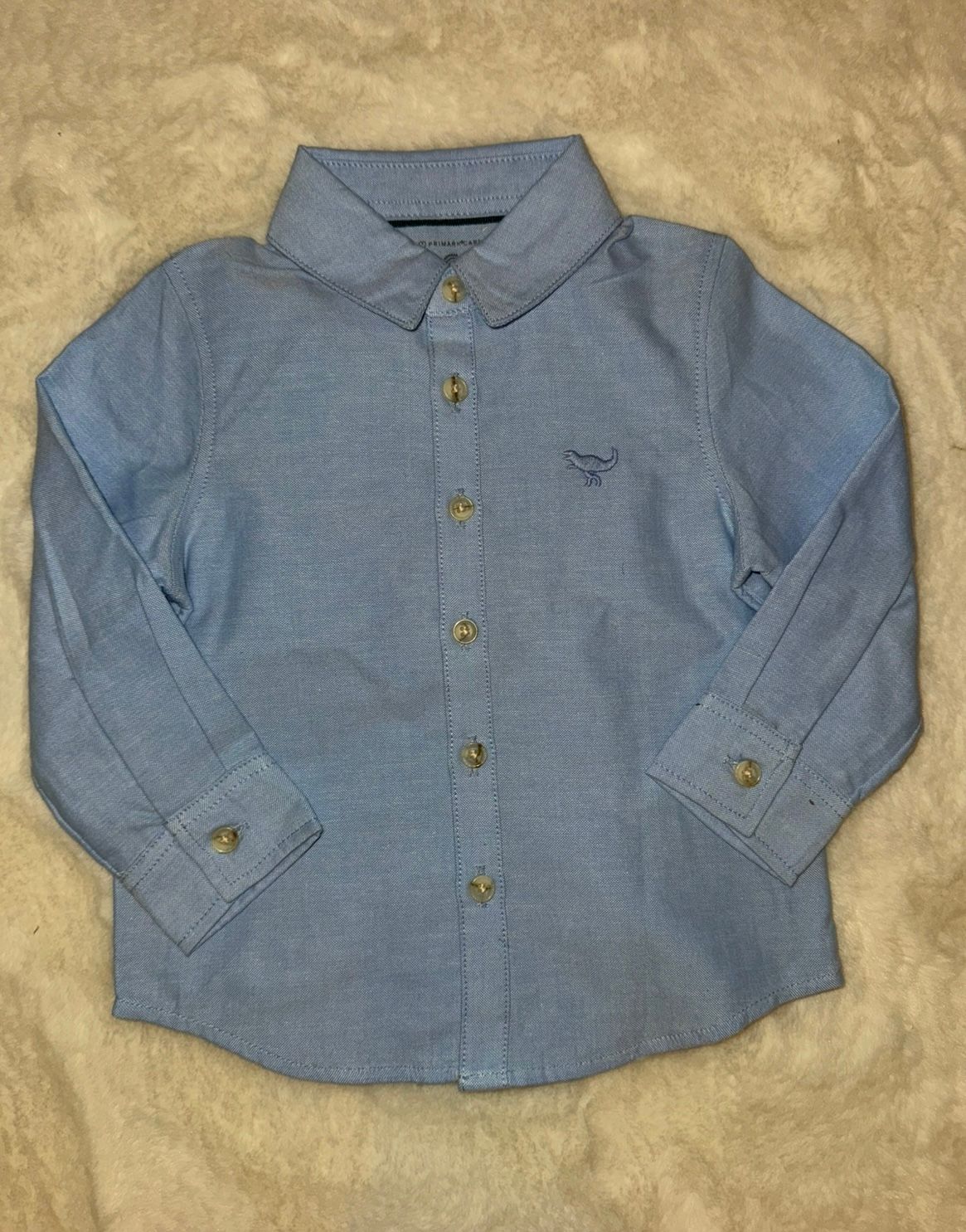 Light blue chambray button-down shirt with long sleeves laid flat.