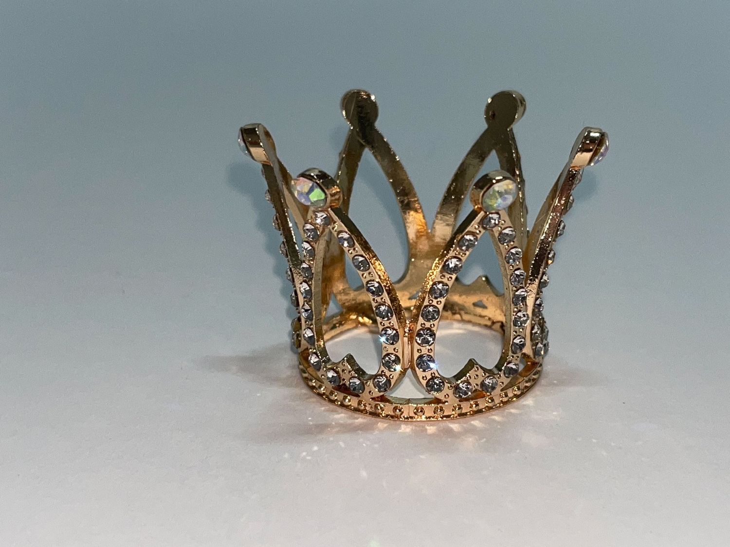 Ornate golden crown with jewels and intricate metalwork details displayed against a light gray background.