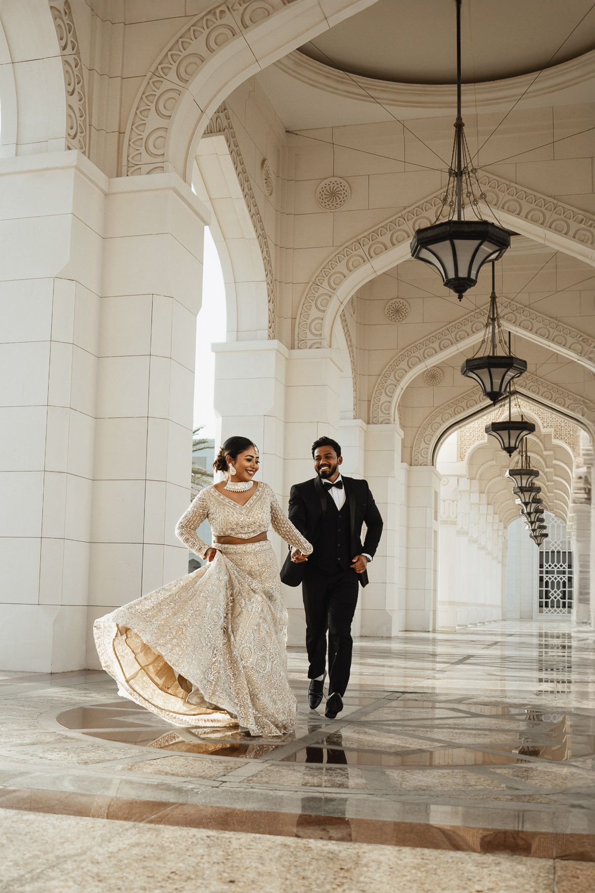 Elegant bride and groom walking beneath grand white arches in Dubai