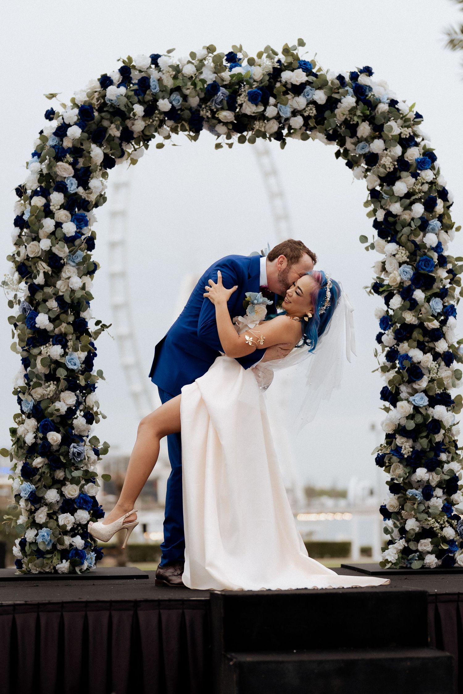 Bride and groom kissing under floral wedding arch during outdoor Dubai wedding ceremony