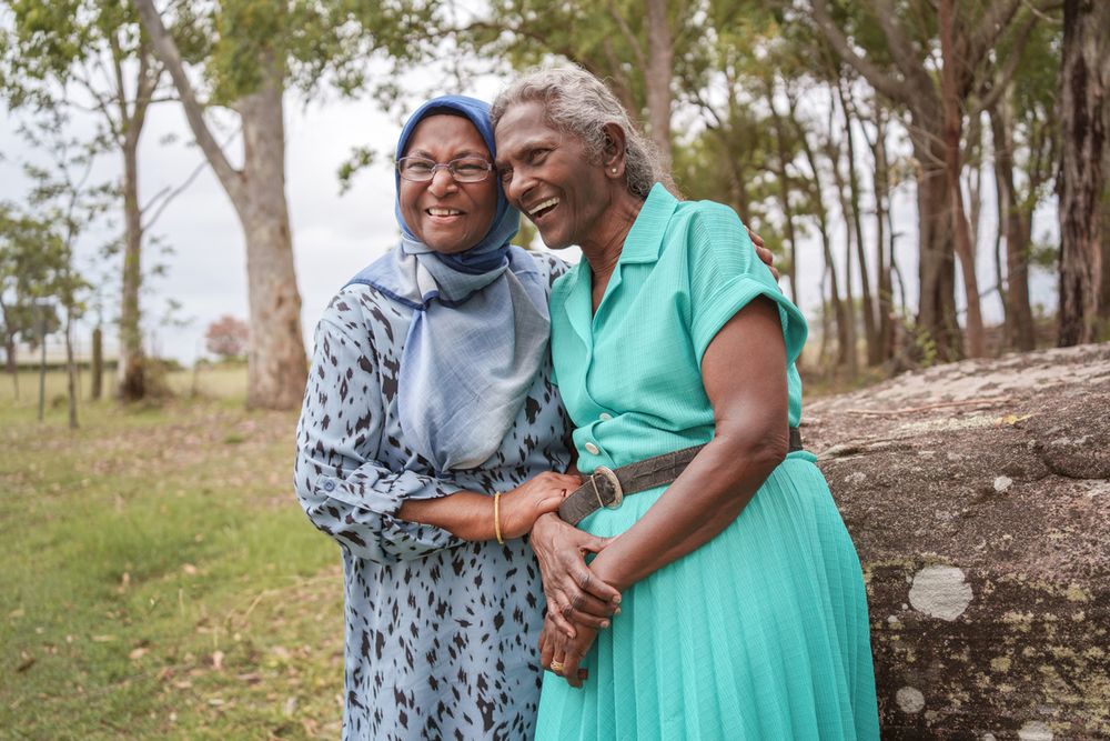 sisters laughing outdoors, one wearing a hijab and one in a teal dress, with trees in the background in rouse hill family photoshoot