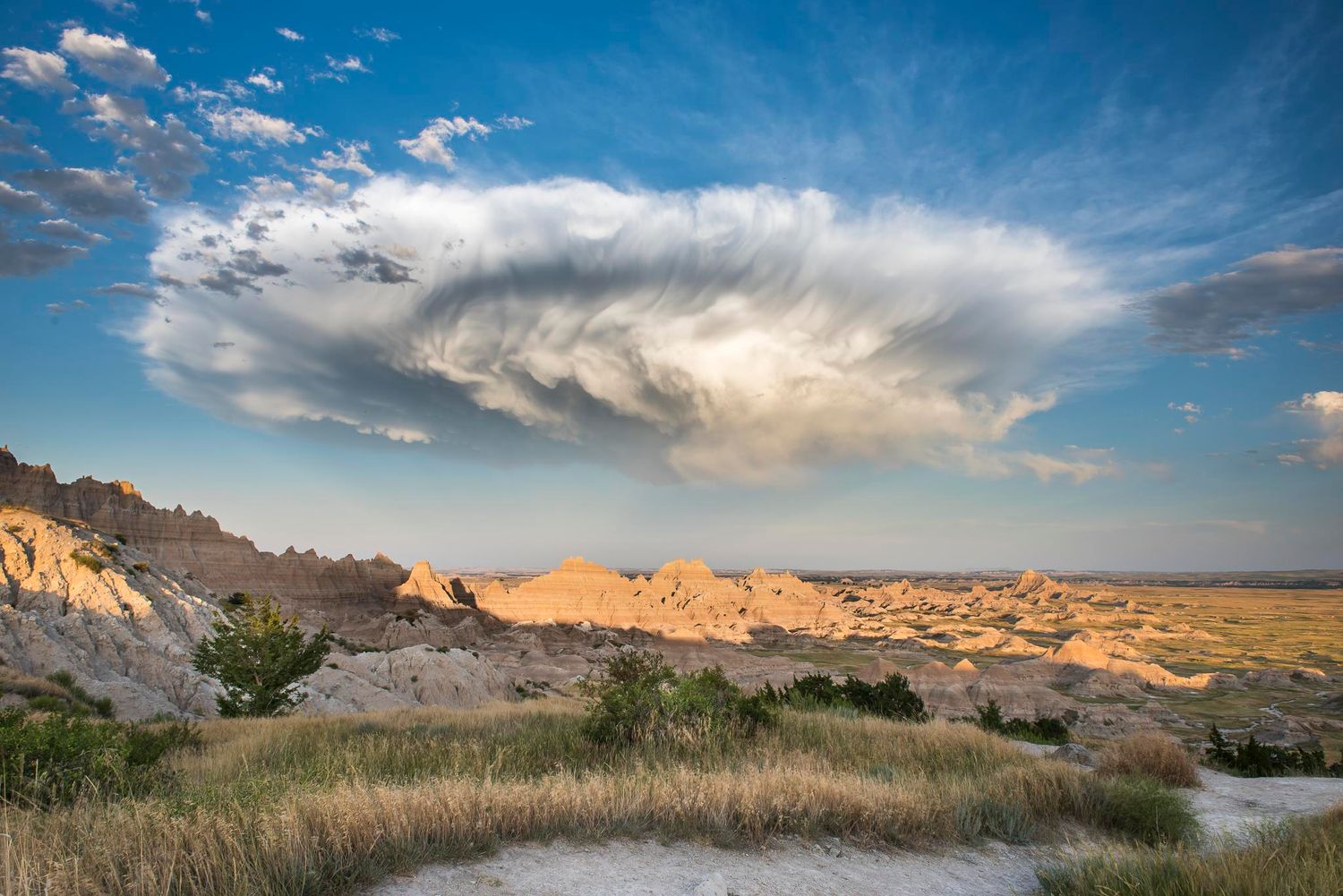 Dramatic storm clouds sweep across a rugged badlands landscape during golden hour.