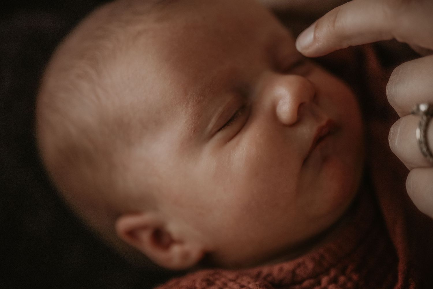 Close up view of a sleeping newborn baby in a soft pink knit wrap.
