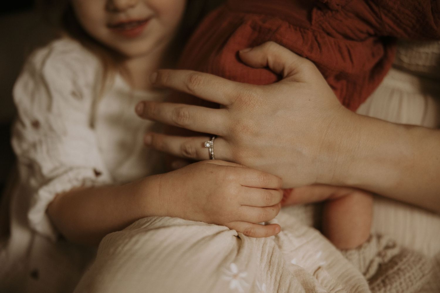 Close-up shot of hands with a wedding ring resting on white lace fabric in soft lighting.