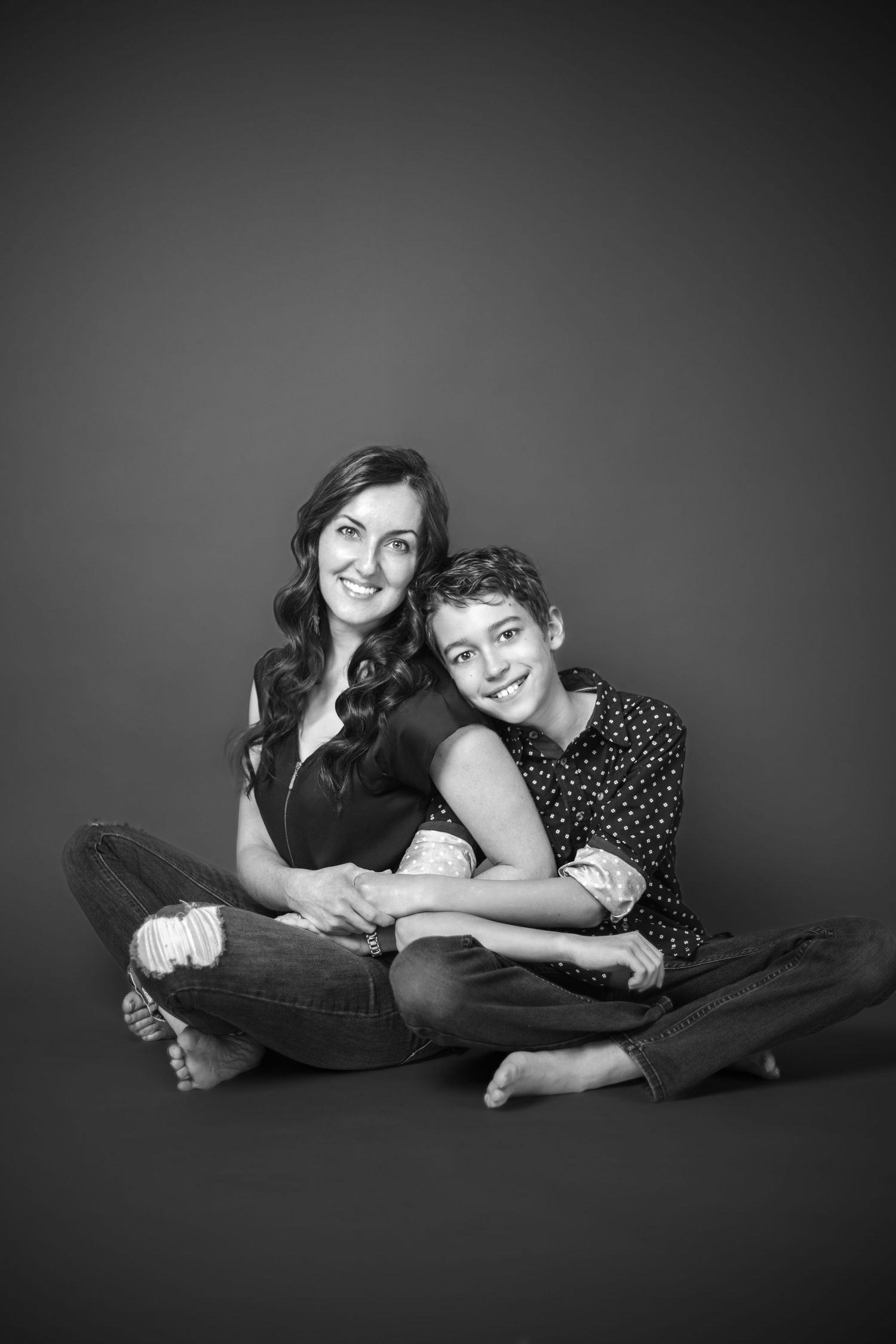 A black and white studio portrait of two people sitting close together on the floor, wearing casual clothing.