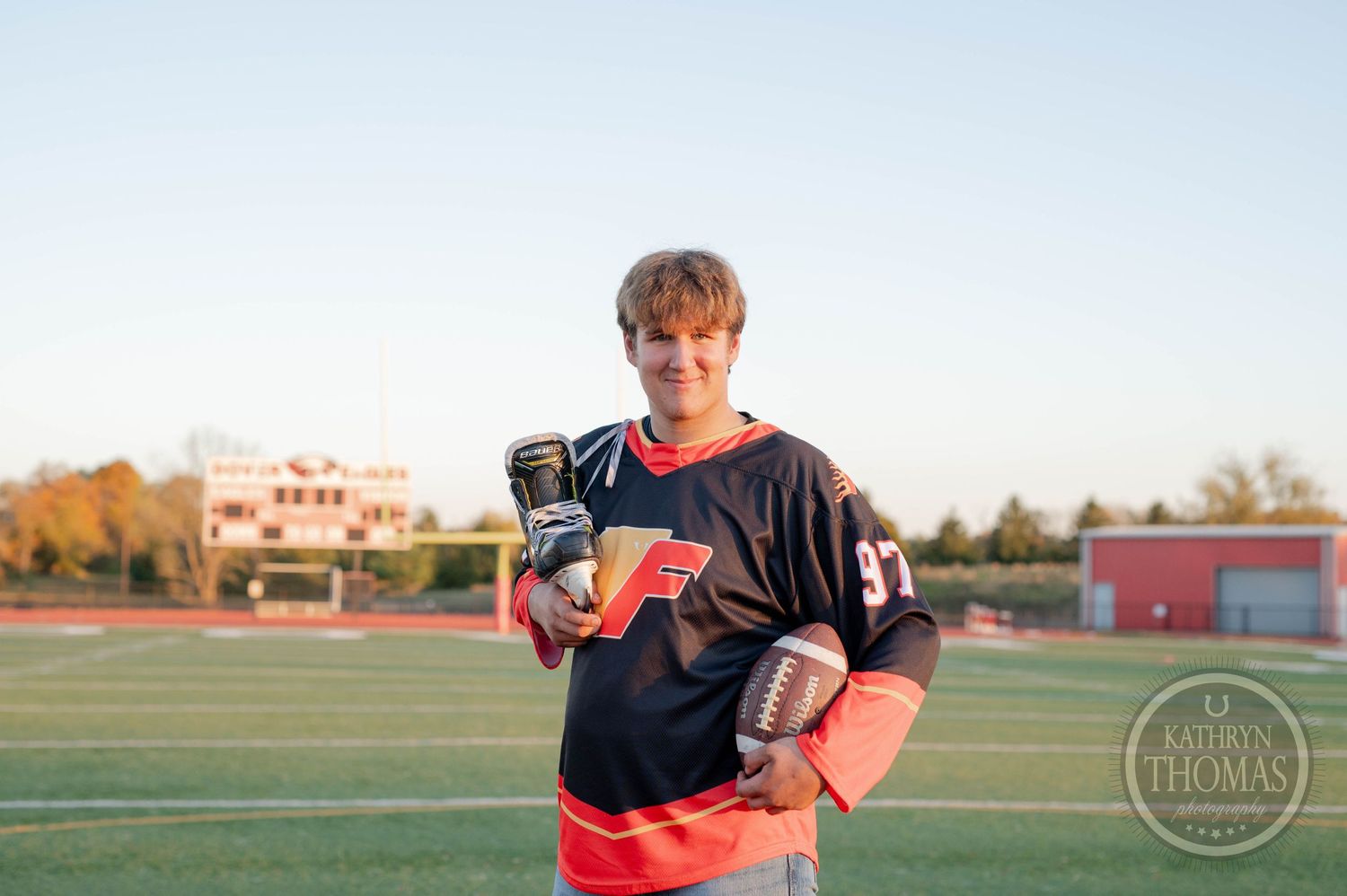 Football player in a black jersey and red pants poses on a sports field at sunset.