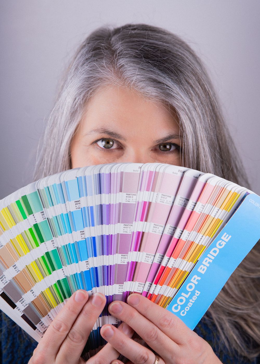 A graphic designer holds a fanned out Pantone color book, partly obscuring her face, for a fun and creative professional headshot.