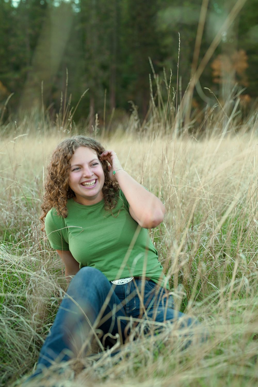 A joyful portrait in tall autumn grass with a relaxed casual pose in a green shirt and jeans.
