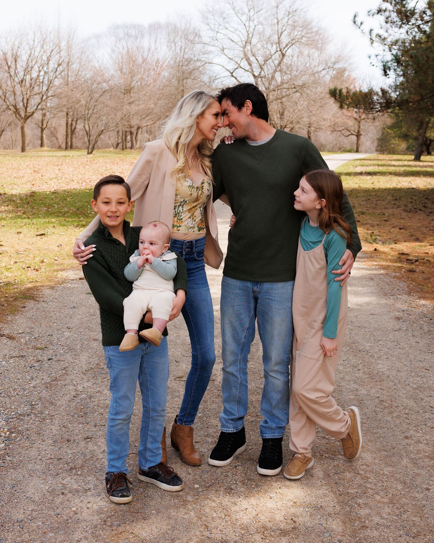 Family of five standing together on a dirt path surrounded by bare winter trees in a park.
