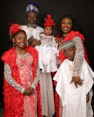 A family poses in coordinating red and white traditional outfits against a dark studio backdrop for a formal portrait.