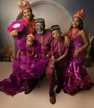 A family portrait session featuring coordinated burgundy outfits with vibrant purple feather boa accents against a neutral backdrop.