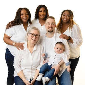A large family group wearing coordinated white outfits poses together for a casual studio portrait against a light background.