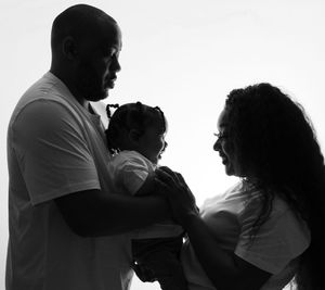 Black and white silhouette of parents holding their small child together in tender family moment.