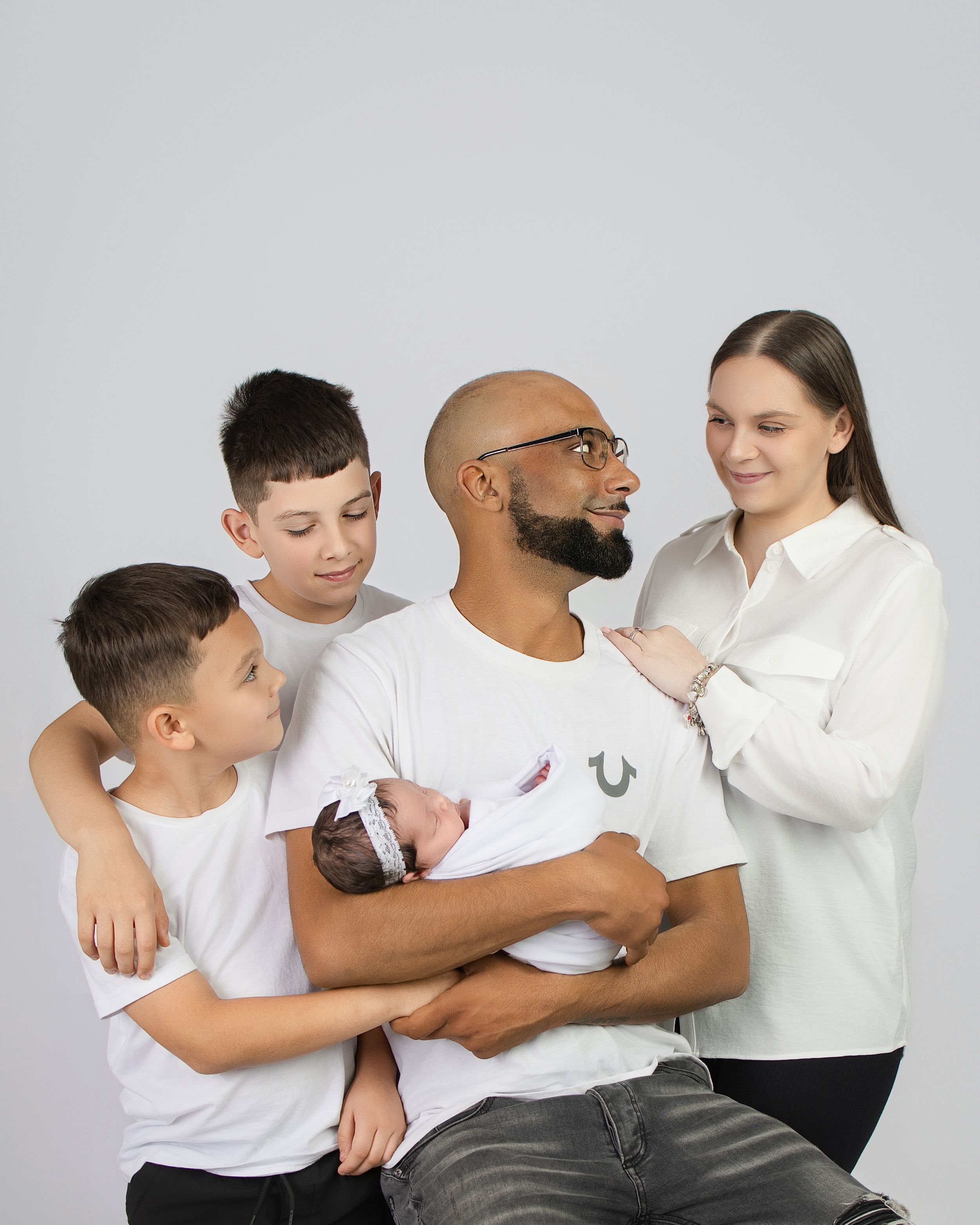 A happy family group in white shirts sits together against a gray background, sharing a warm moment.