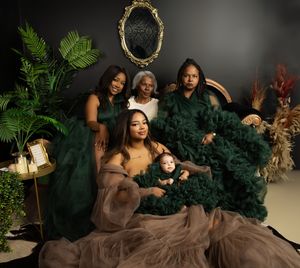A multi-generational group poses in coordinating formal dresses of emerald green and taupe with decorative elements.