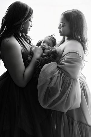A black and white artistic portrait of two people cradling a newborn baby in an intimate moment.