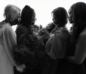 Black and white silhouette of a group gathering around and gazing lovingly at a small baby in a tender moment.
