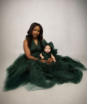 A figure in an elegant emerald green gown poses with a small child in a matching outfit against a light background.