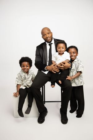 A family portrait featuring a parent and three young children wearing coordinated black and white outfits against a white backdrop.