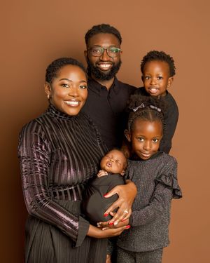 Beautiful family portrait of five people wearing coordinated dark outfits posing against a warm brown background.