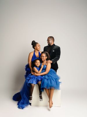 A family wearing matching royal blue tulle skirts and black tops poses together in a studio against a white backdrop.